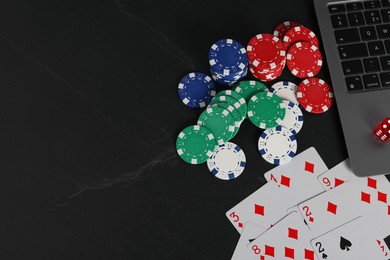 Photo of Online poker. Playing cards, chips, dice and laptop on black table, top view. Space for text