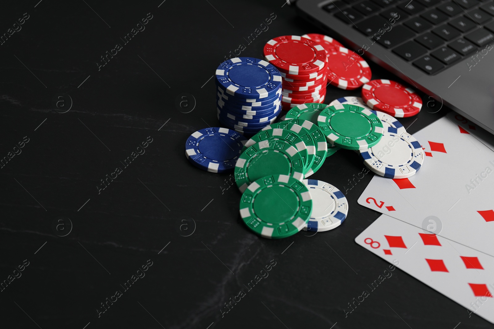 Photo of Online poker. Playing cards, chips and laptop on black table, closeup. Space for text