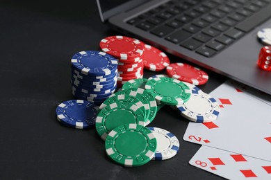 Photo of Online poker. Playing cards, chips and laptop on black table, closeup