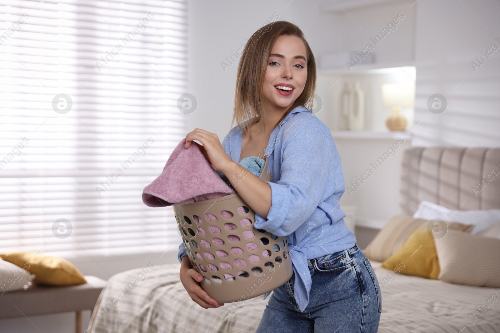 Photo of Happy young housewife with basket full of laundry at home