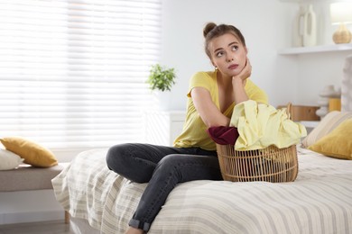 Photo of Tired housewife with basket full of laundry on bed at home