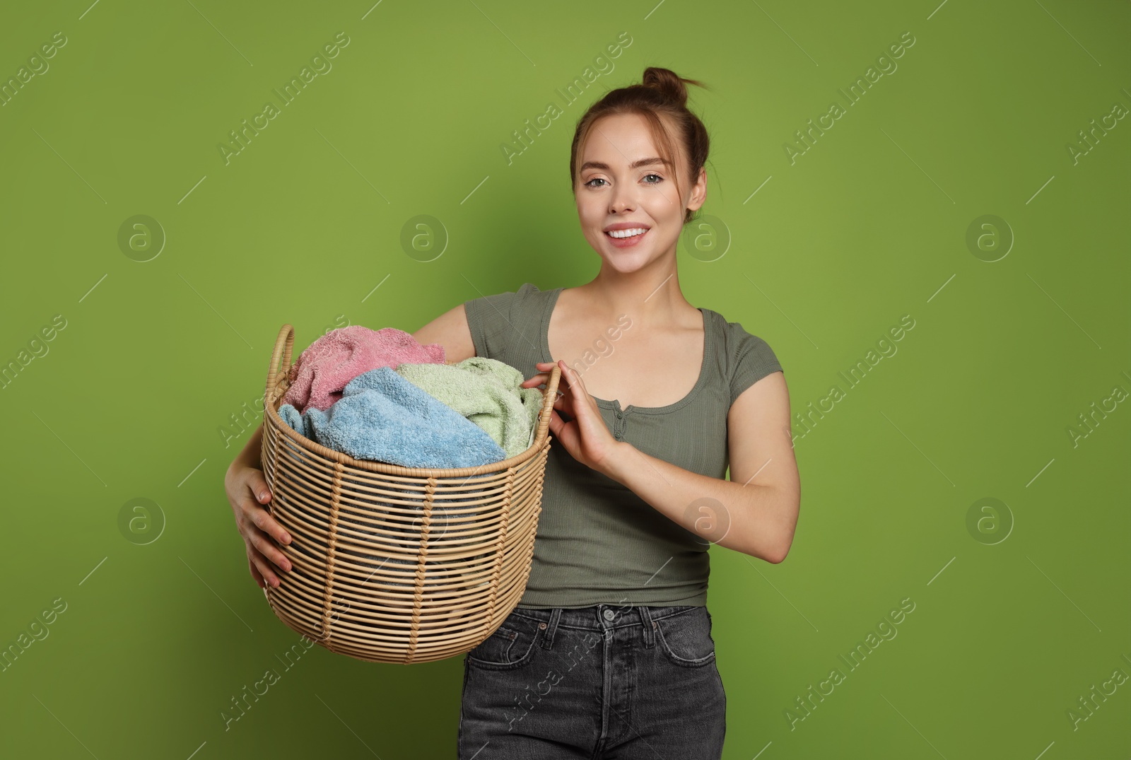 Photo of Happy young housewife with basket full of laundry on olive background