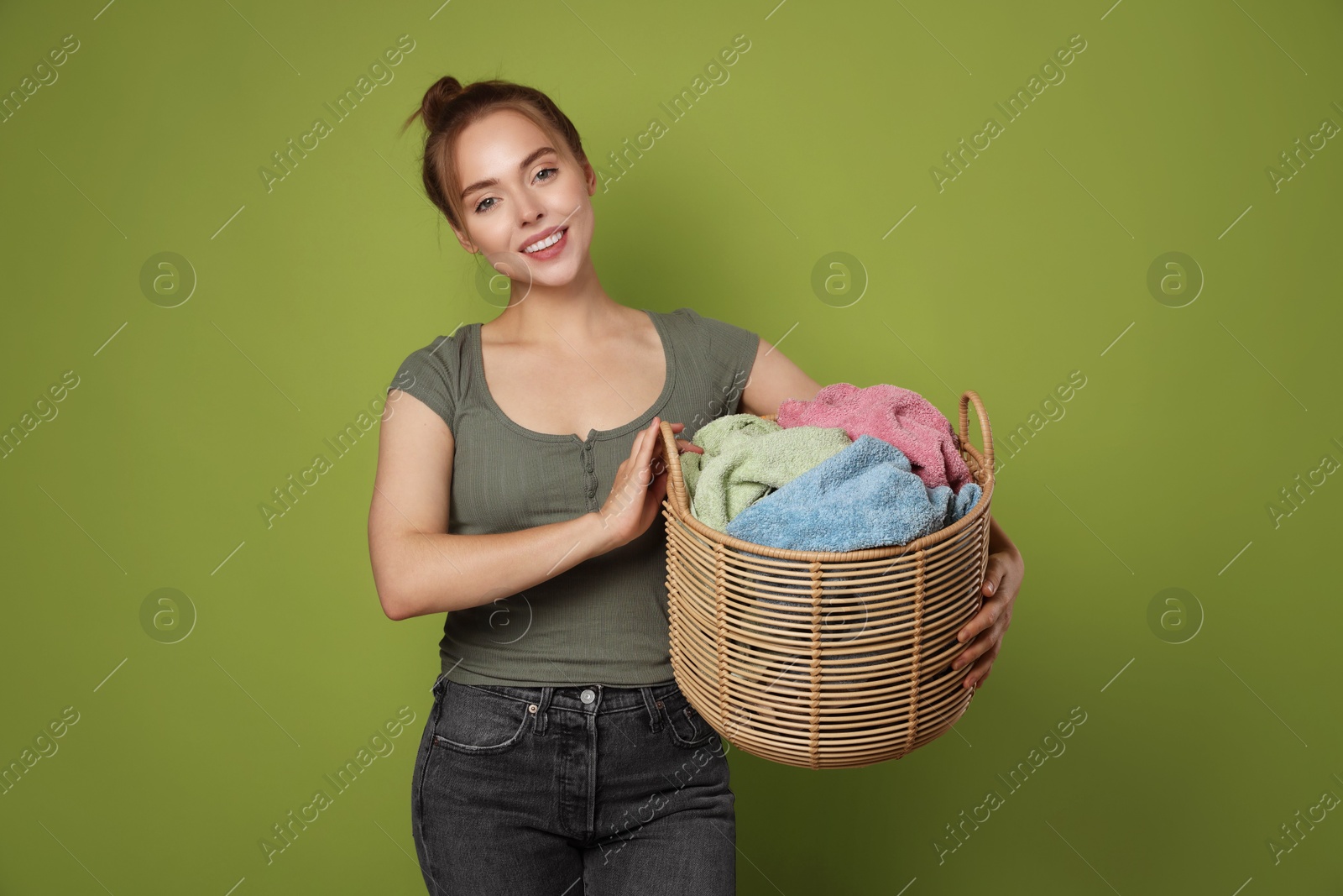 Photo of Happy young housewife with basket full of laundry on olive background