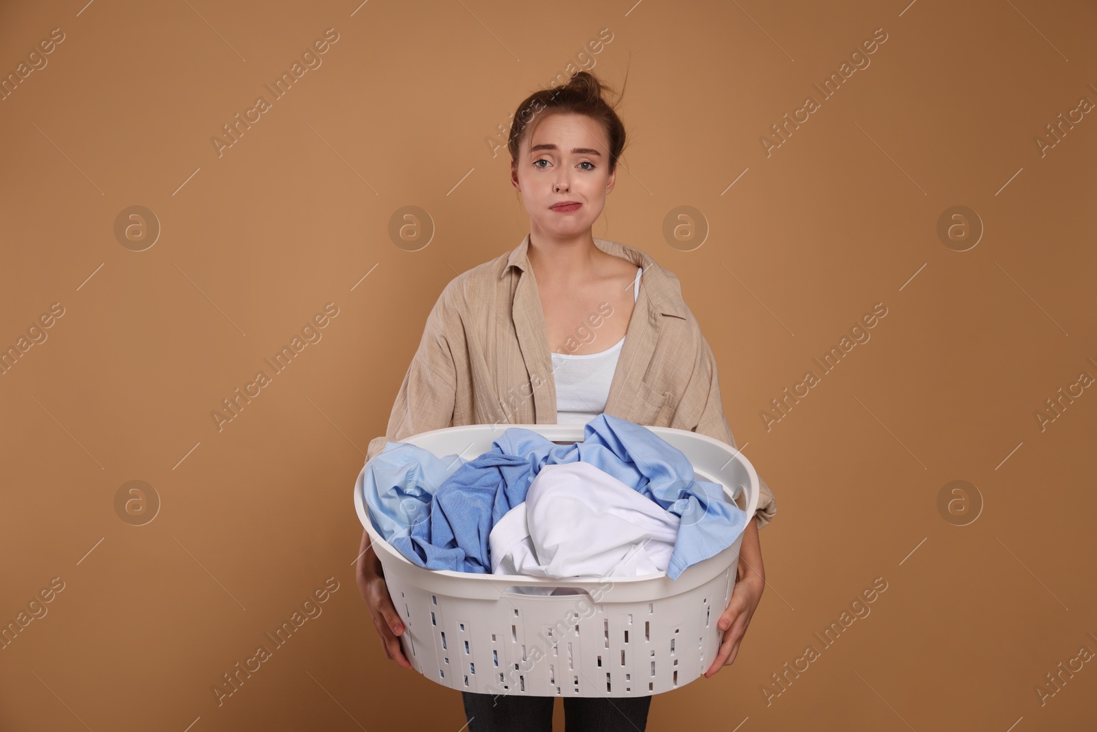 Photo of Tired housewife with basket full of laundry on pale orange background