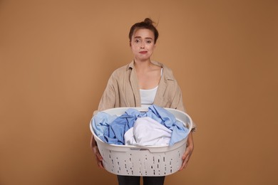 Tired housewife with basket full of laundry on pale orange background