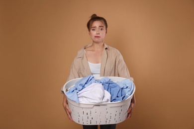 Photo of Tired housewife with basket full of laundry on pale orange background