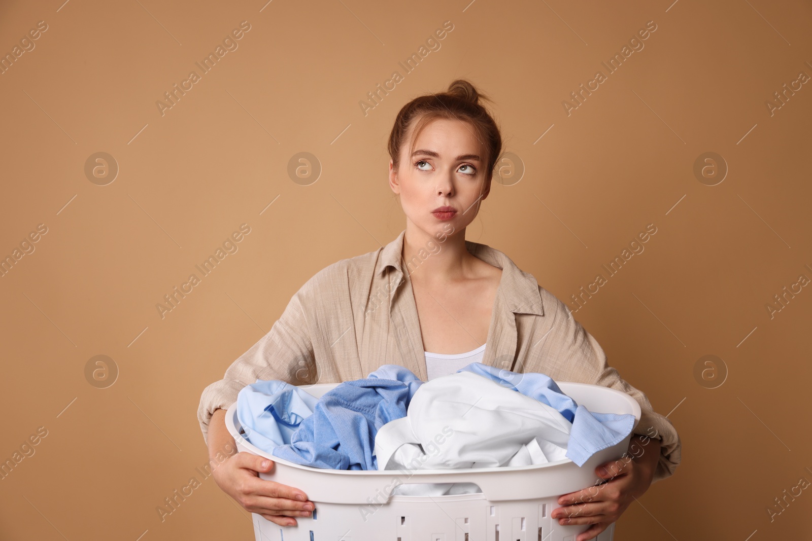 Photo of Tired housewife with basket full of laundry on pale orange background