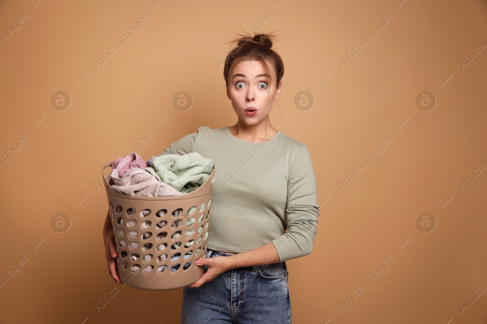 Photo of Emotional housewife with basket full of laundry on pale orange background