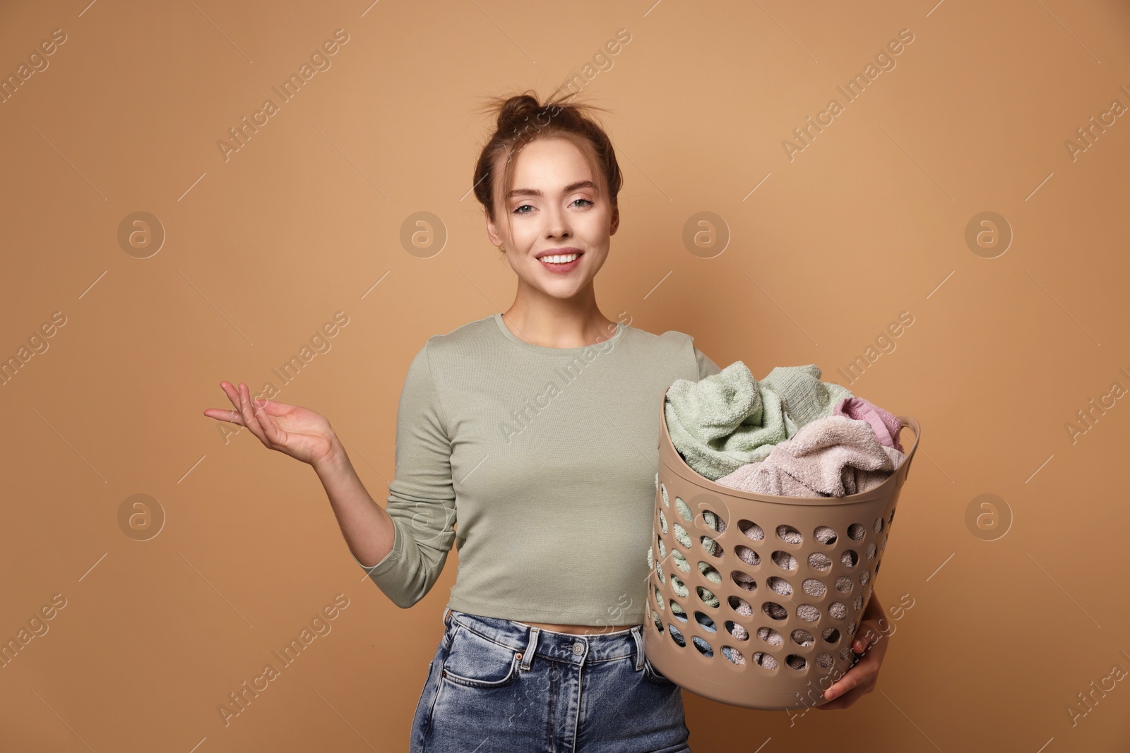 Photo of Happy young housewife with basket full of laundry on pale orange background