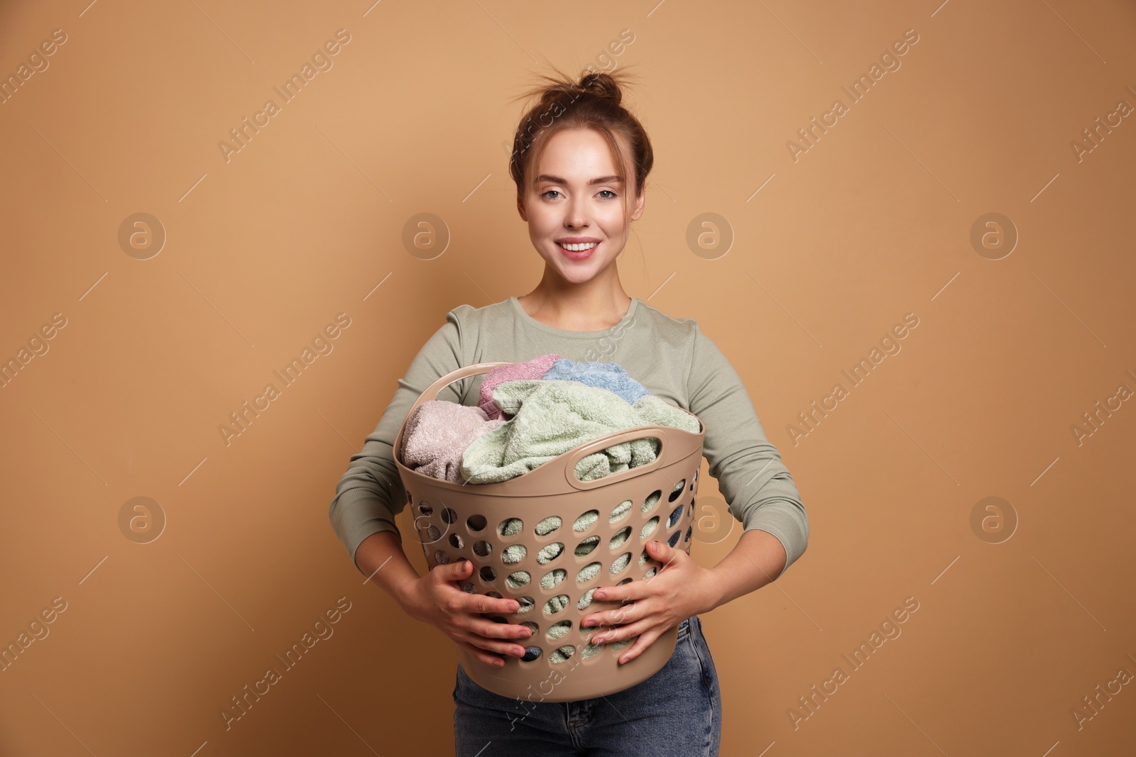 Photo of Happy young housewife with basket full of laundry on pale orange background