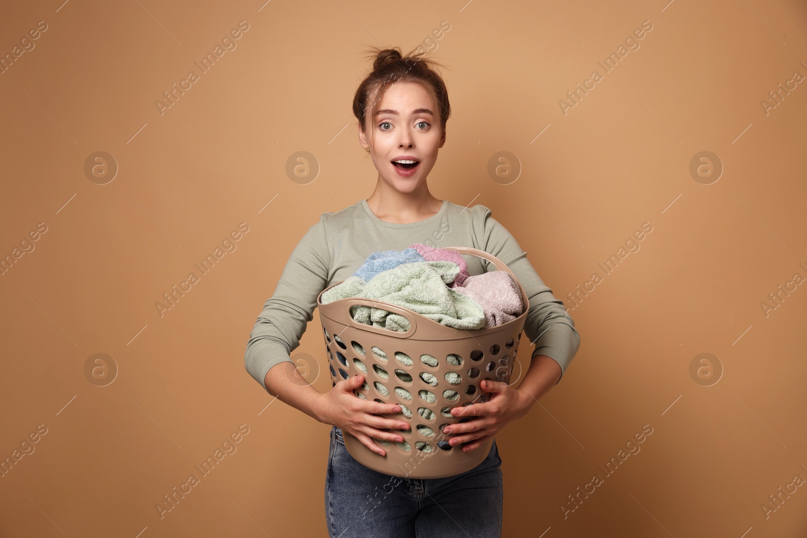 Photo of Happy young housewife with basket full of laundry on pale orange background