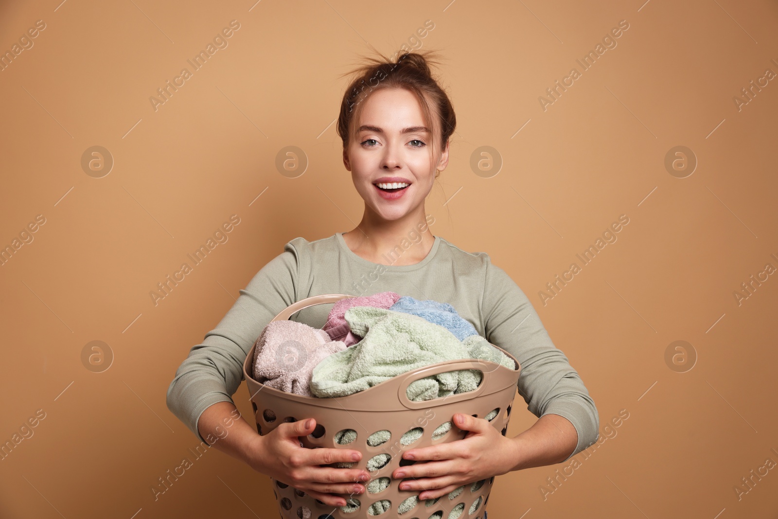 Photo of Happy young housewife with basket full of laundry on pale orange background