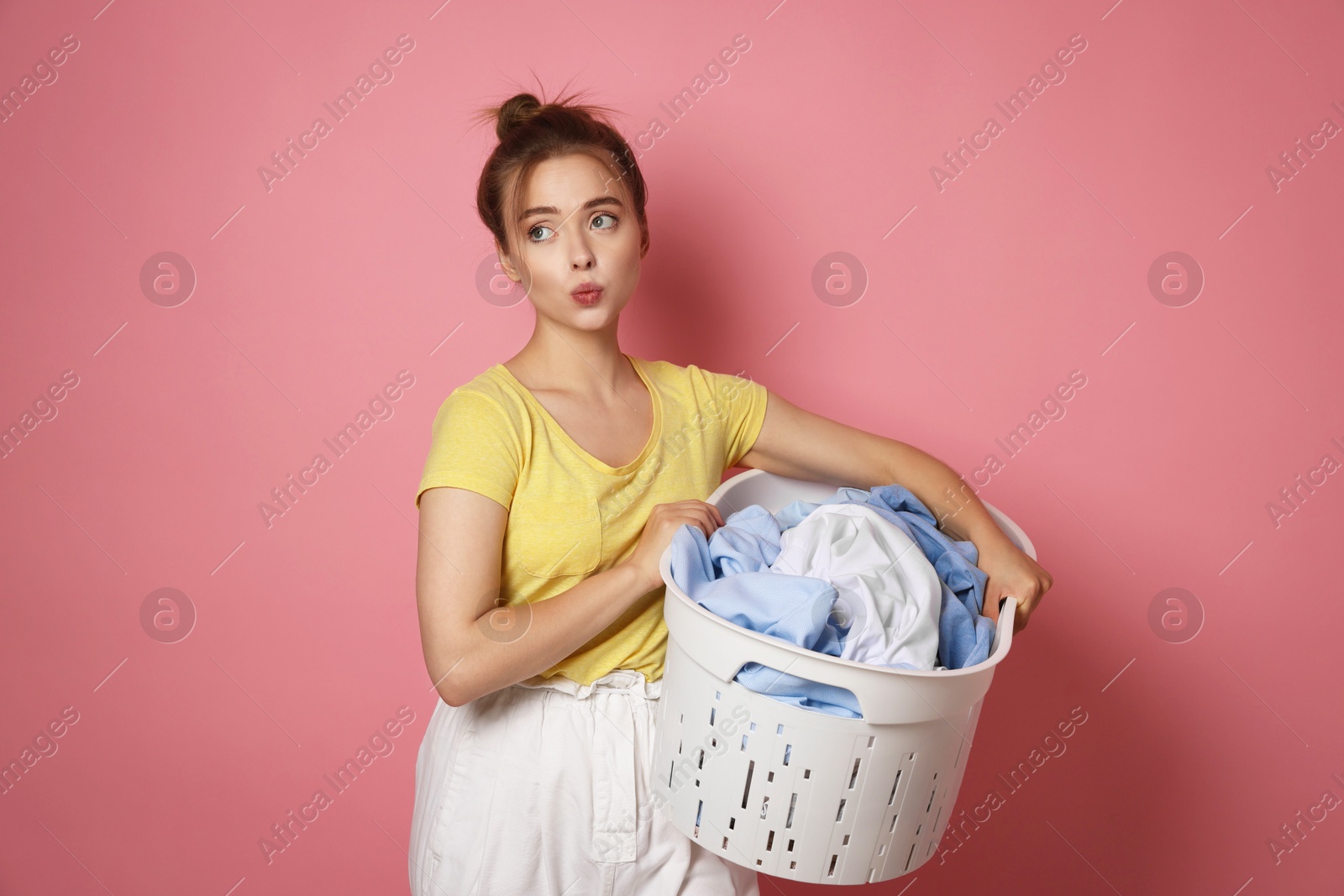 Photo of Young housewife with basket full of laundry on pale pink background