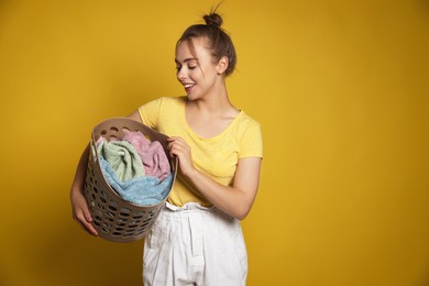 Photo of Happy young housewife with basket full of laundry on yellow background. Space for text