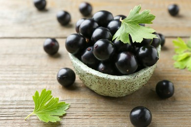 Photo of Fresh ripe black currant berries and leaves on wooden table, closeup