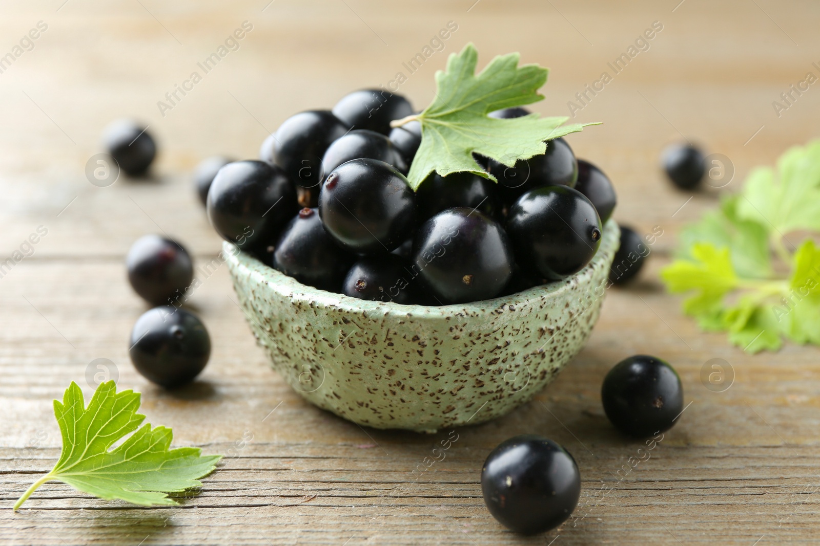 Photo of Fresh ripe black currant berries and leaves on wooden table, closeup