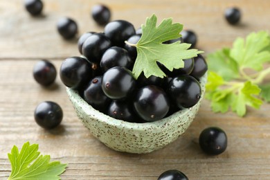 Photo of Fresh ripe black currant berries and leaves on wooden table, closeup