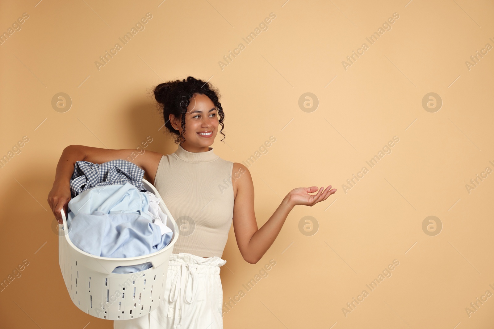 Photo of Happy woman with basket full of laundry on beige background, space for text