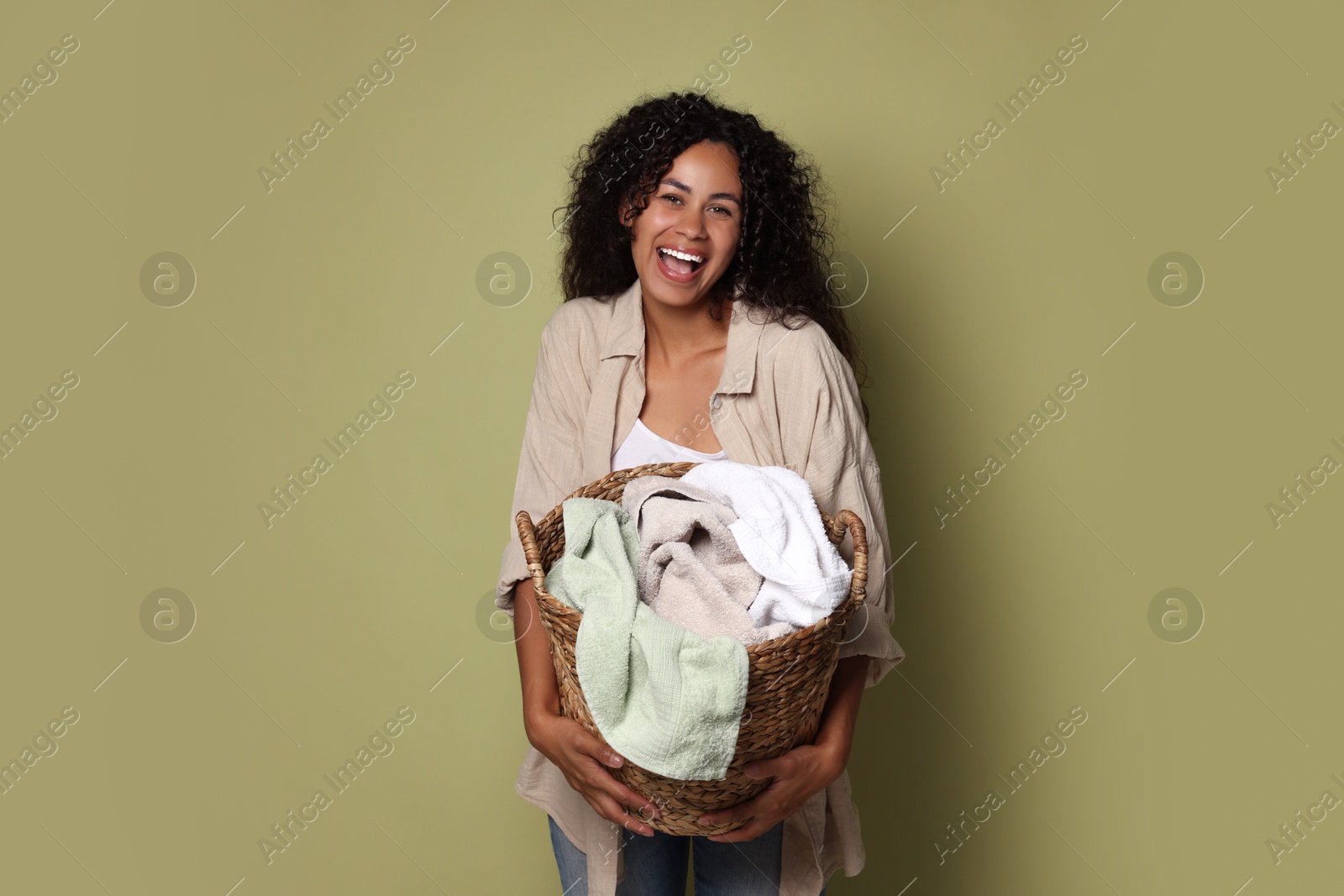 Photo of Happy woman with basket full of laundry on olive background