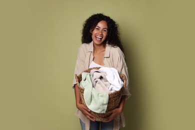 Photo of Happy woman with basket full of laundry on olive background