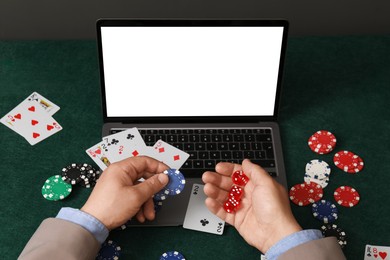 Photo of Online poker. Man holding chips and dice at green table with laptop, closeup