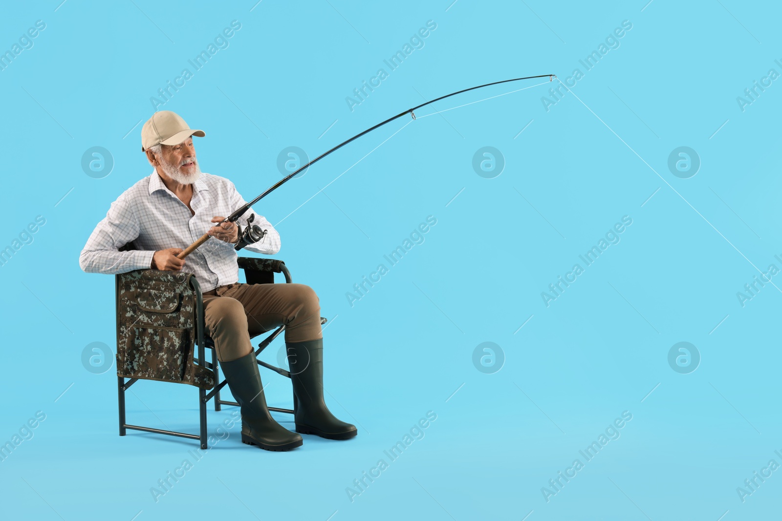 Photo of Fisherman with rod on fishing chair against light blue background