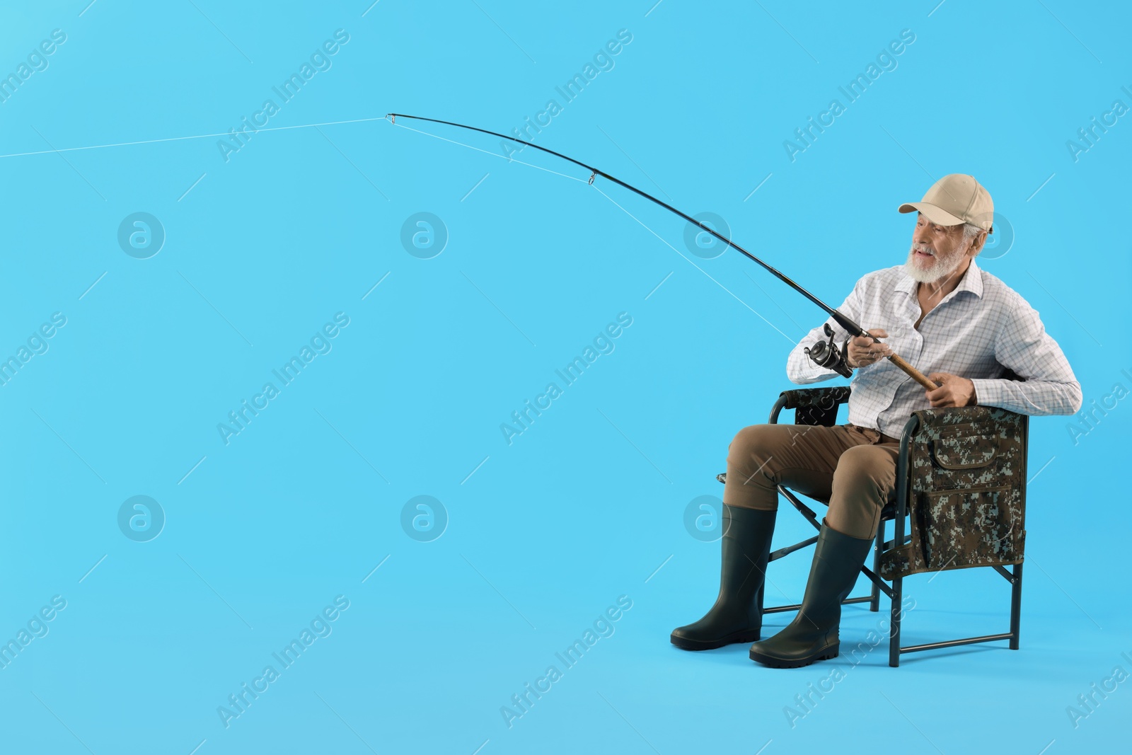 Photo of Fisherman with rod on fishing chair against light blue background