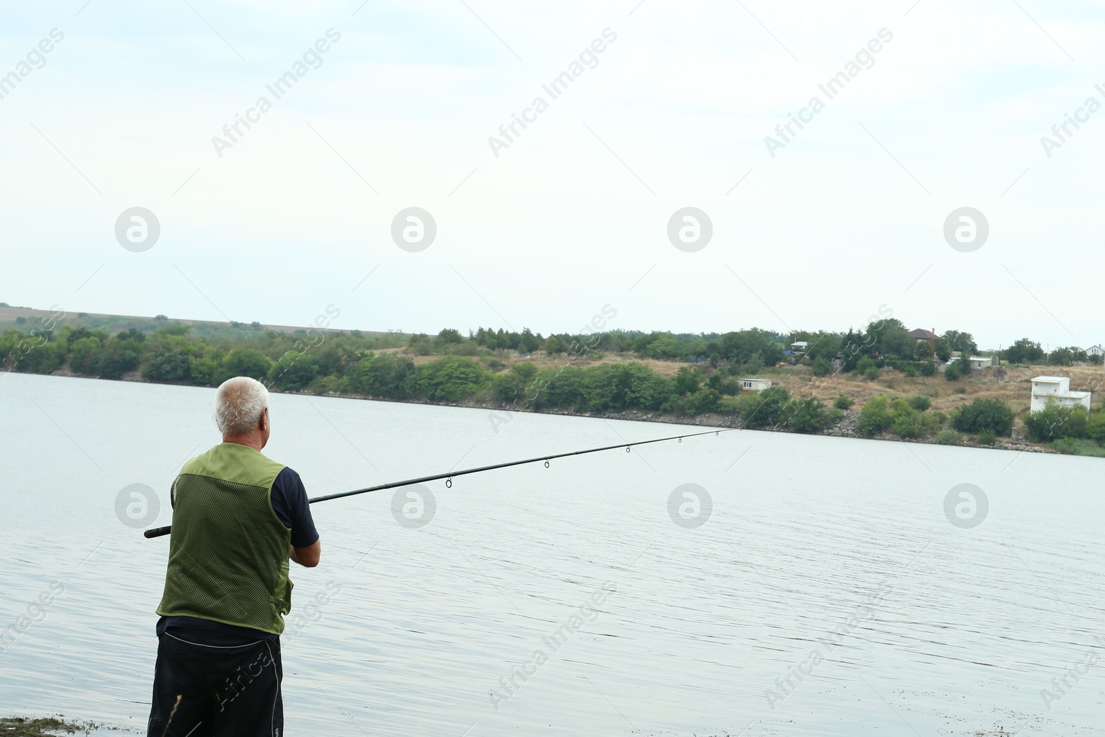 Photo of Fisherman with rod fishing near lake at summer, back view