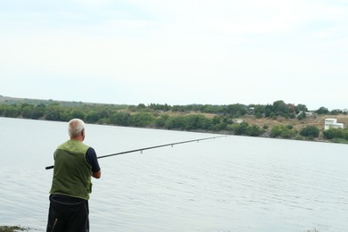 Fisherman with rod fishing near lake at summer, back view