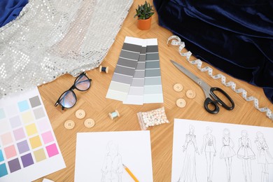 Photo of Sketches of stylish clothes, color palettes and other fashion designer`s supplies on wooden table, above view