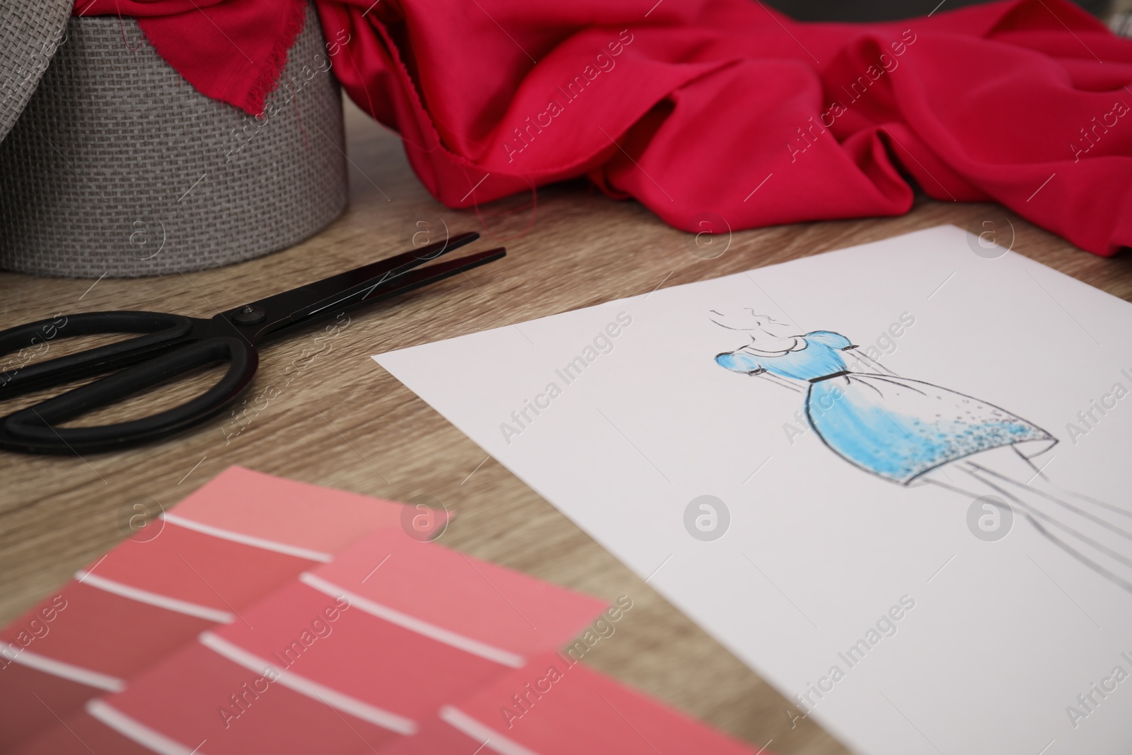 Photo of Sketch of stylish dress and other fashion designer`s supplies on wooden table, closeup