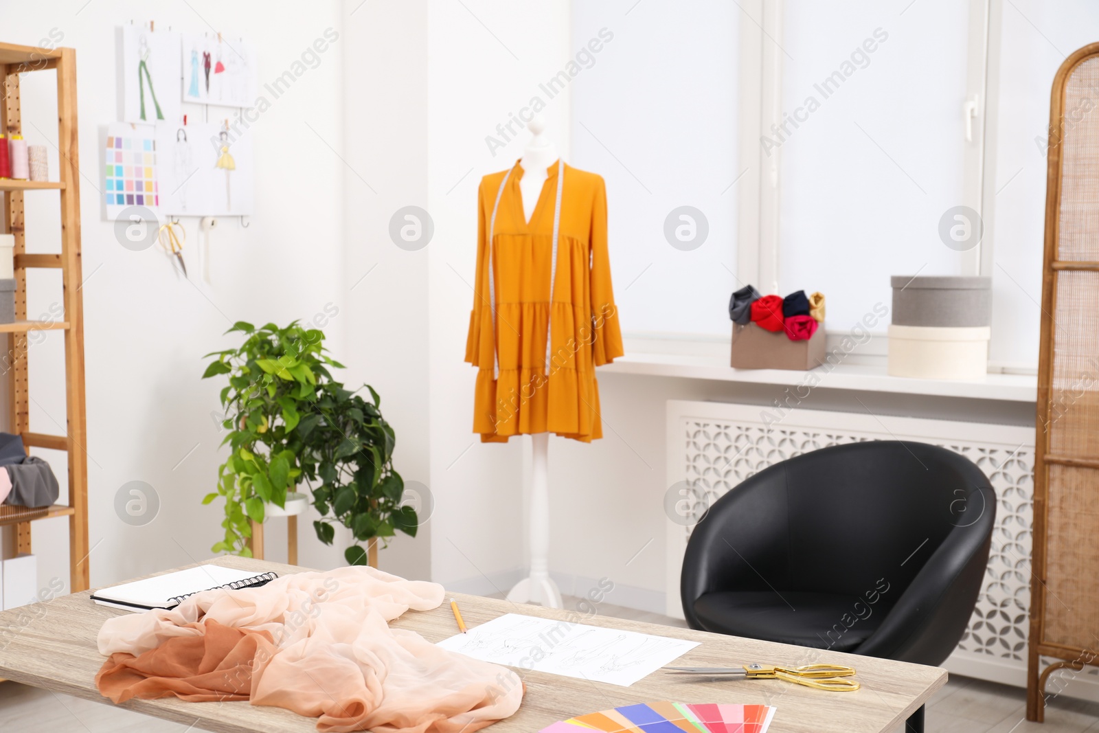 Photo of Different fashion designer`s supplies on wooden table and mannequin with new dress in workshop