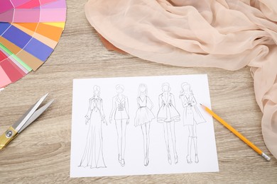 Photo of Sketch of stylish clothes and other fashion designer`s supplies on wooden table, flat lay