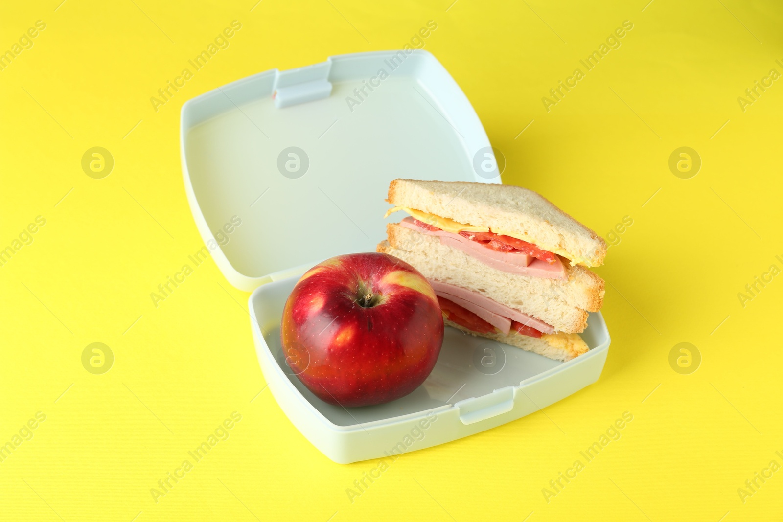 Photo of Lunch box with sandwich and apple on yellow background