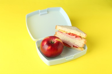 Photo of Lunch box with sandwich and apple on yellow background