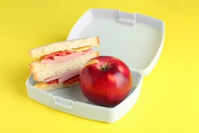 Photo of Lunch box with sandwich and apple on yellow background