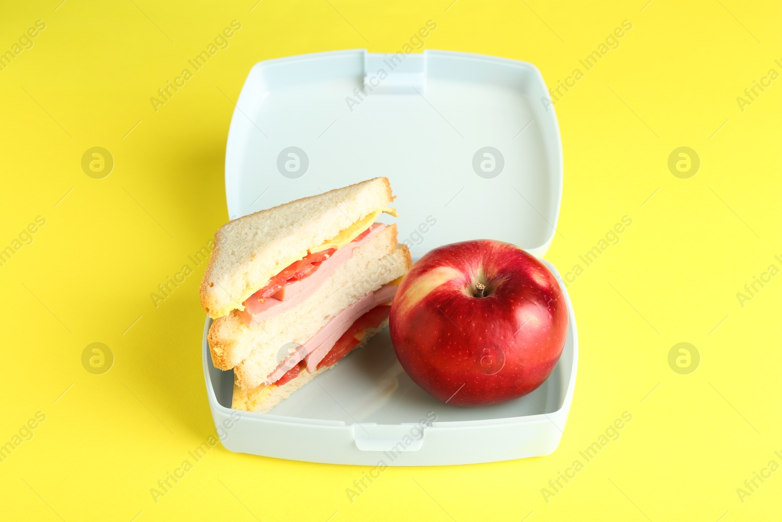 Photo of Lunch box with sandwich and apple on yellow background