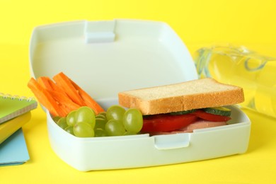 Photo of Lunch box with snacks, bottle of water and alarm clock on yellow background, closeup