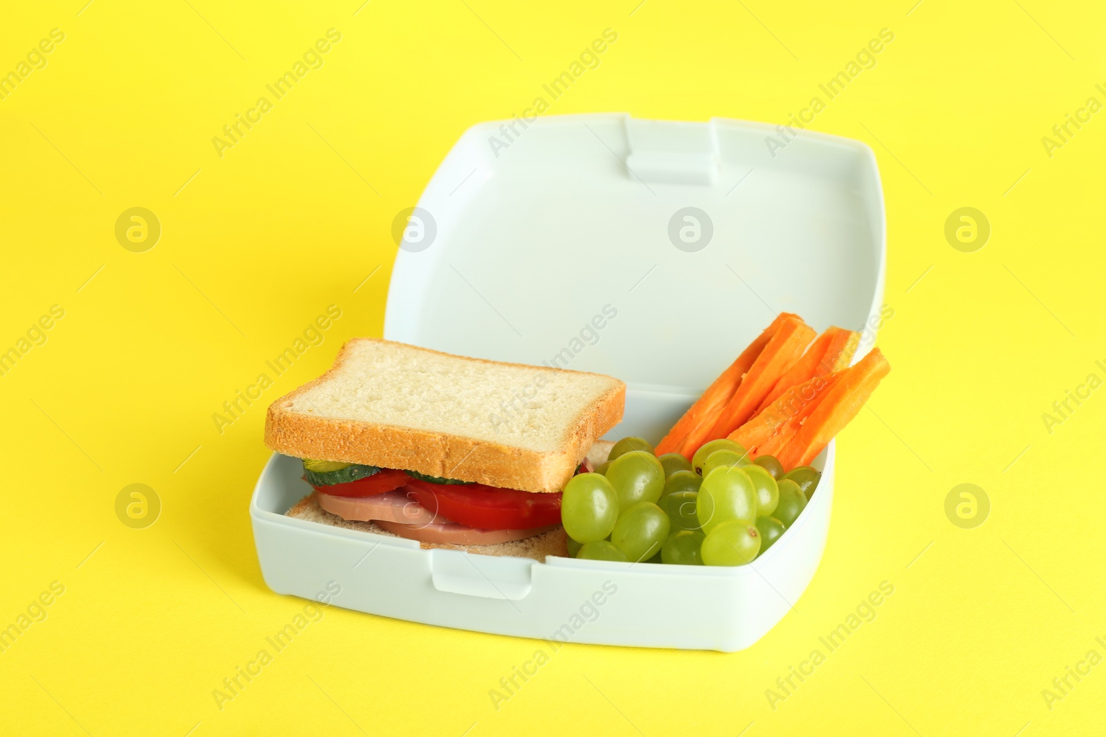 Photo of Lunch box with sandwich, carrot and grape on yellow background