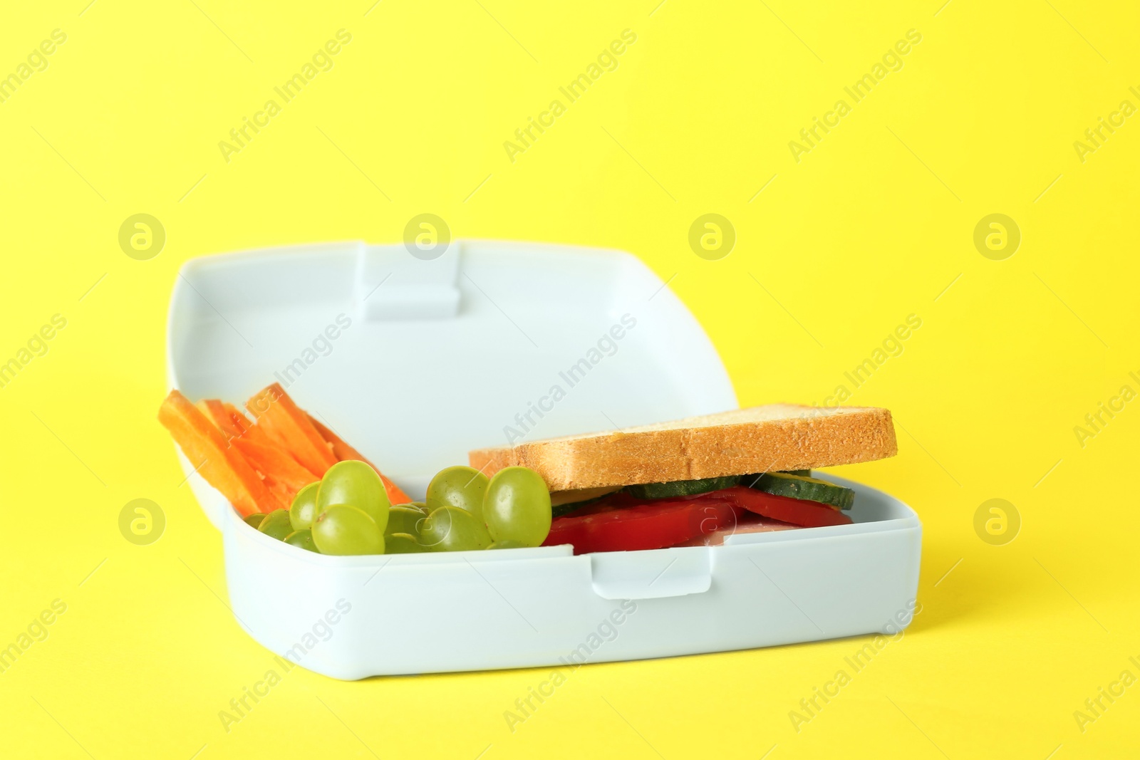 Photo of Lunch box with sandwich, carrot and grape on yellow background