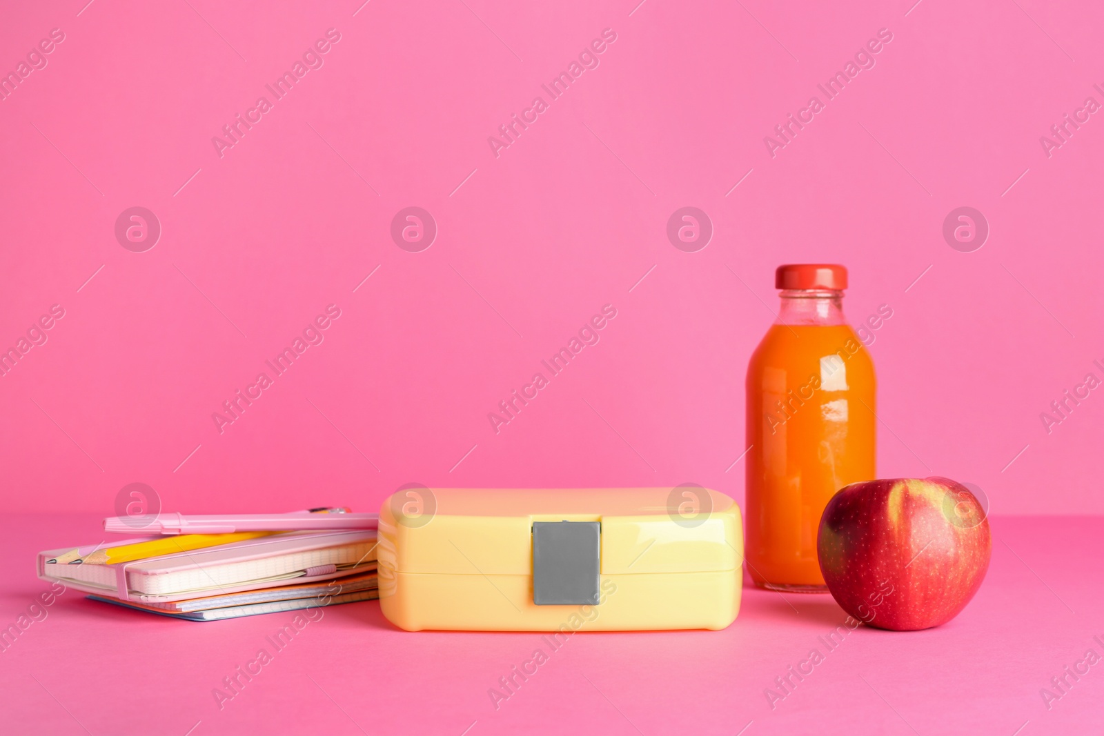 Photo of Lunch box, apple, bottle of juice and stationery on pink background