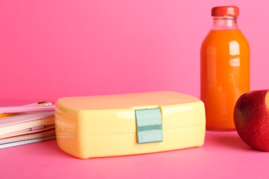 Photo of Lunch box, apple, bottle of juice and stationery on pink background