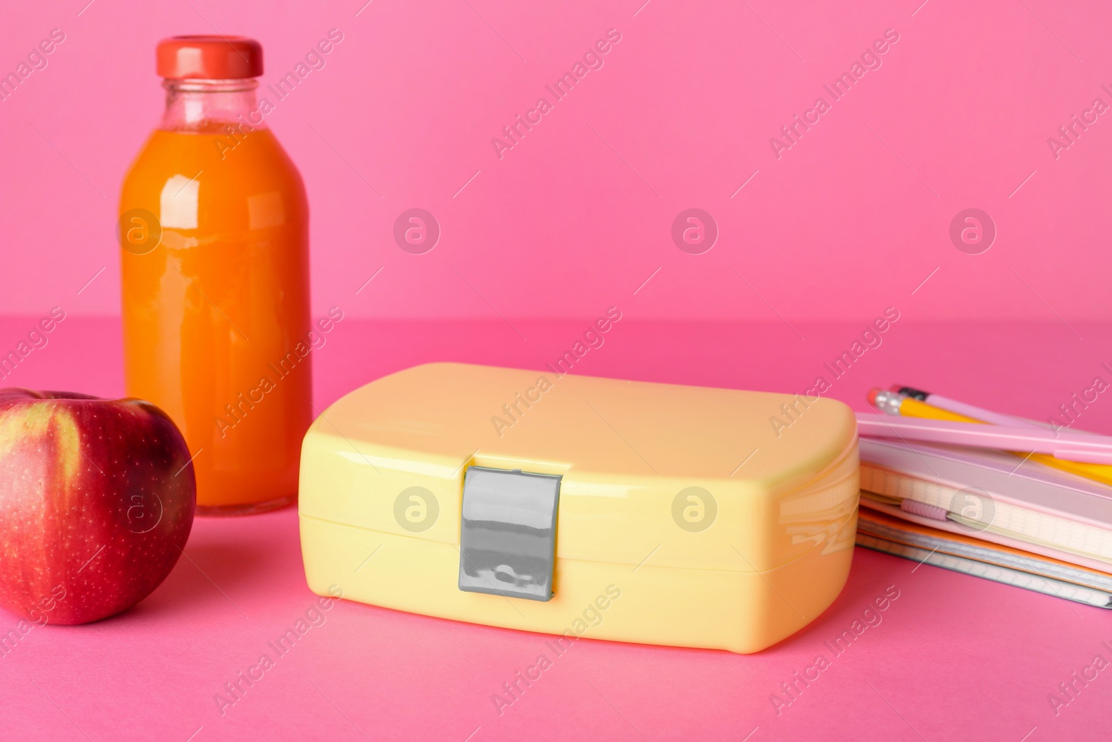 Photo of Lunch box, apple, bottle of juice and stationery on pink background