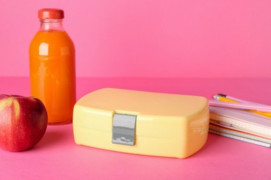 Photo of Lunch box, apple, bottle of juice and stationery on pink background