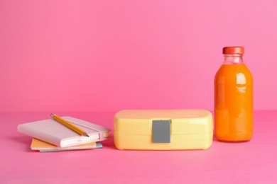 Photo of Lunch box, apple, bottle of juice and stationery on pink background