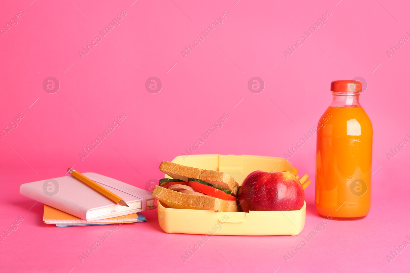 Photo of Lunch box with snacks, bottle of juice and stationery on pink background