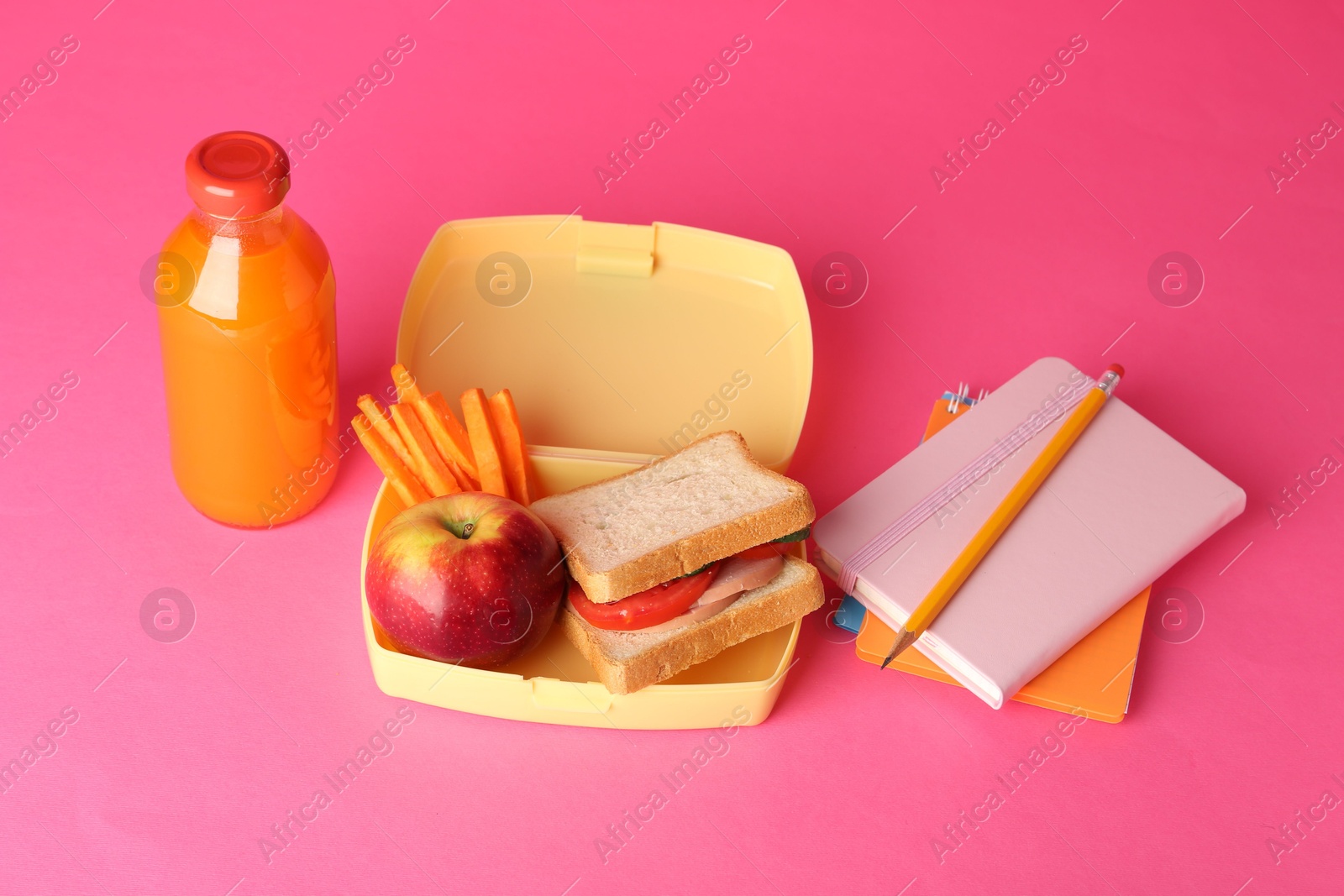 Photo of Lunch box with snacks, bottle of juice and stationery on pink background