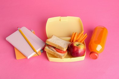 Photo of Lunch box with snacks, bottle of juice and stationery on pink background