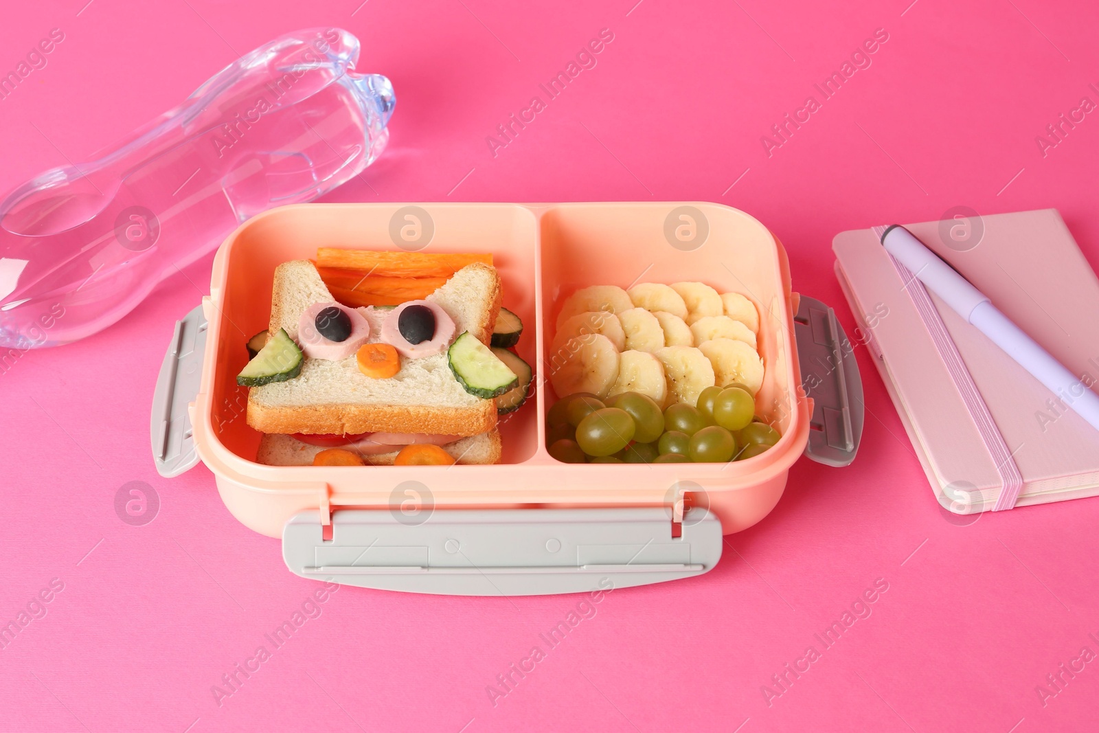 Photo of Lunch box with snacks, bottle of water and stationery on pink background