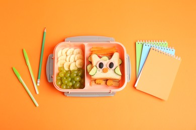 Photo of Lunch box with snacks and stationery on orange background, flat lay